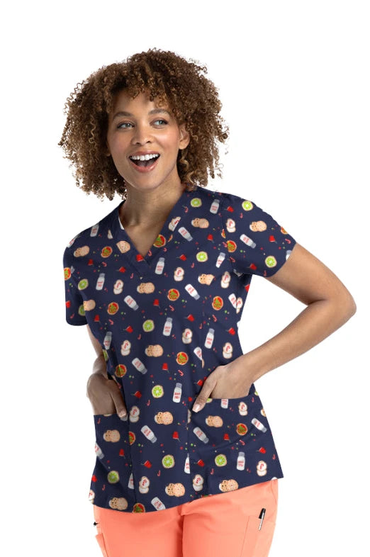 Woman wearing a navy scrub top with colorful pattern and coral pants on a white background